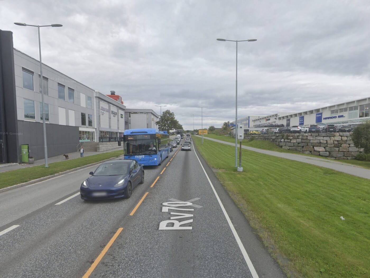 Fixed speed camera beside an urban Norwegian road (Rv70) with daytime traffic.